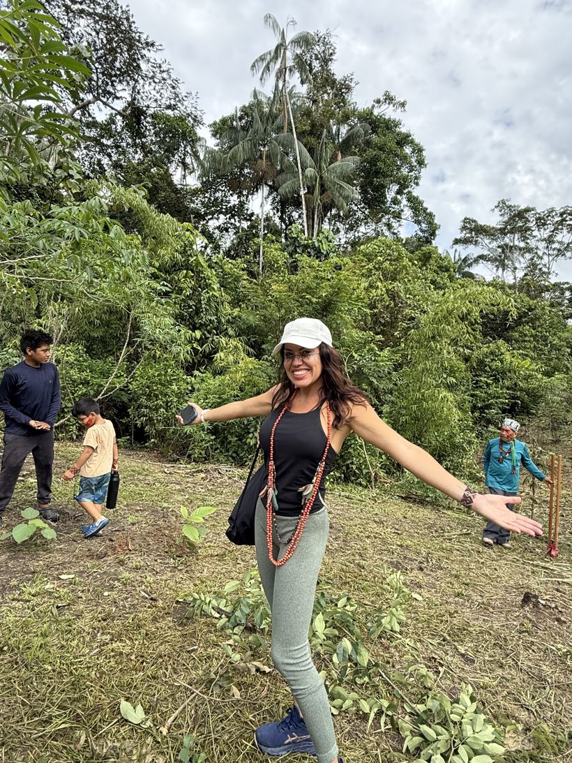 Márcia smiling with open arms in the cleared planting ground, with young cacao seedlings and members of the community around her