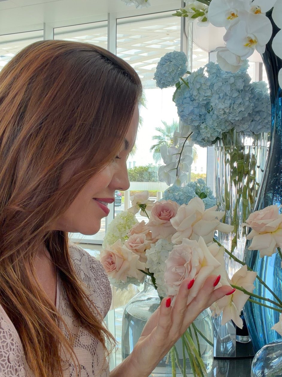 Márcia arranging white orchids and pale roses in a tall glass vase