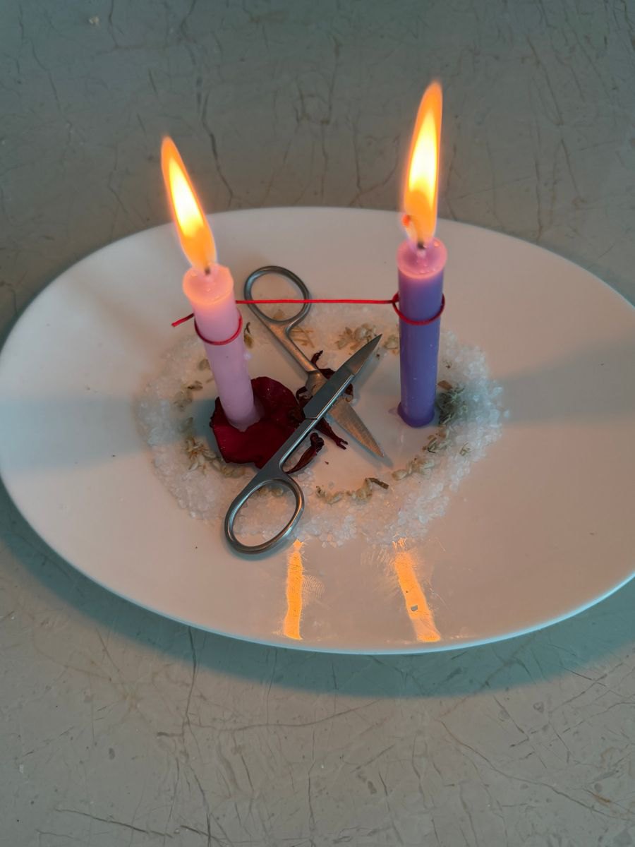 Two candles joined by a red thread on a white plate, with scissors resting beside them